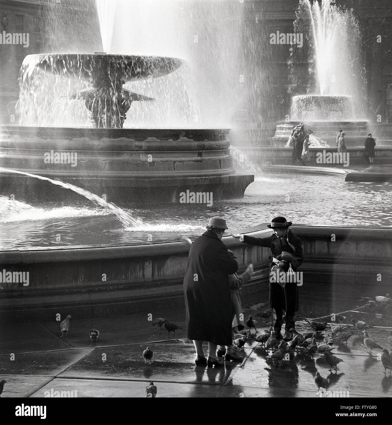 Immagine storica degli anni '50 di questa epoca di una nonna con i suoi nipoti che nutrono alcuni piccioni presso le fontane a Trafalgar Square, Londra, Inghilterra, Regno Unito. Foto Stock