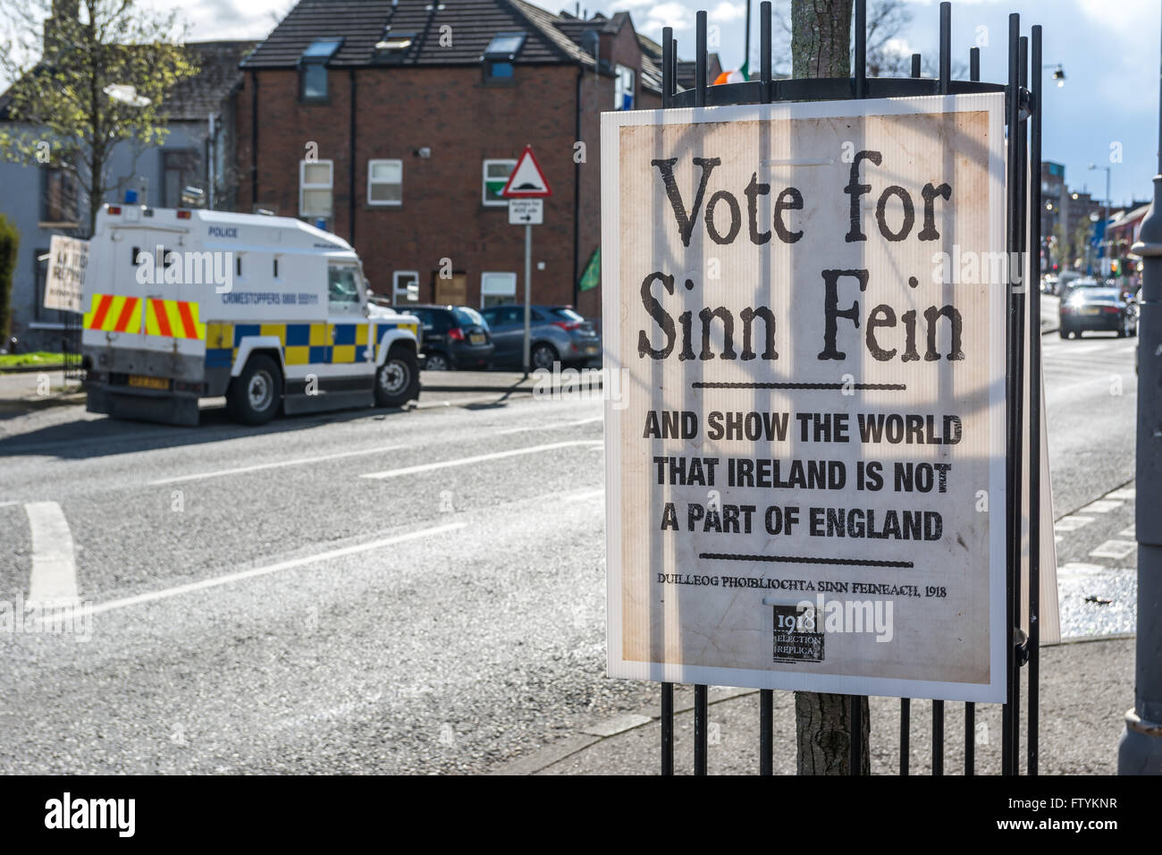 Votare per il Sinn Fein cartellone elettorale su Belfast's Falls Road con PSNI land rover parcheggiato in background. Foto Stock