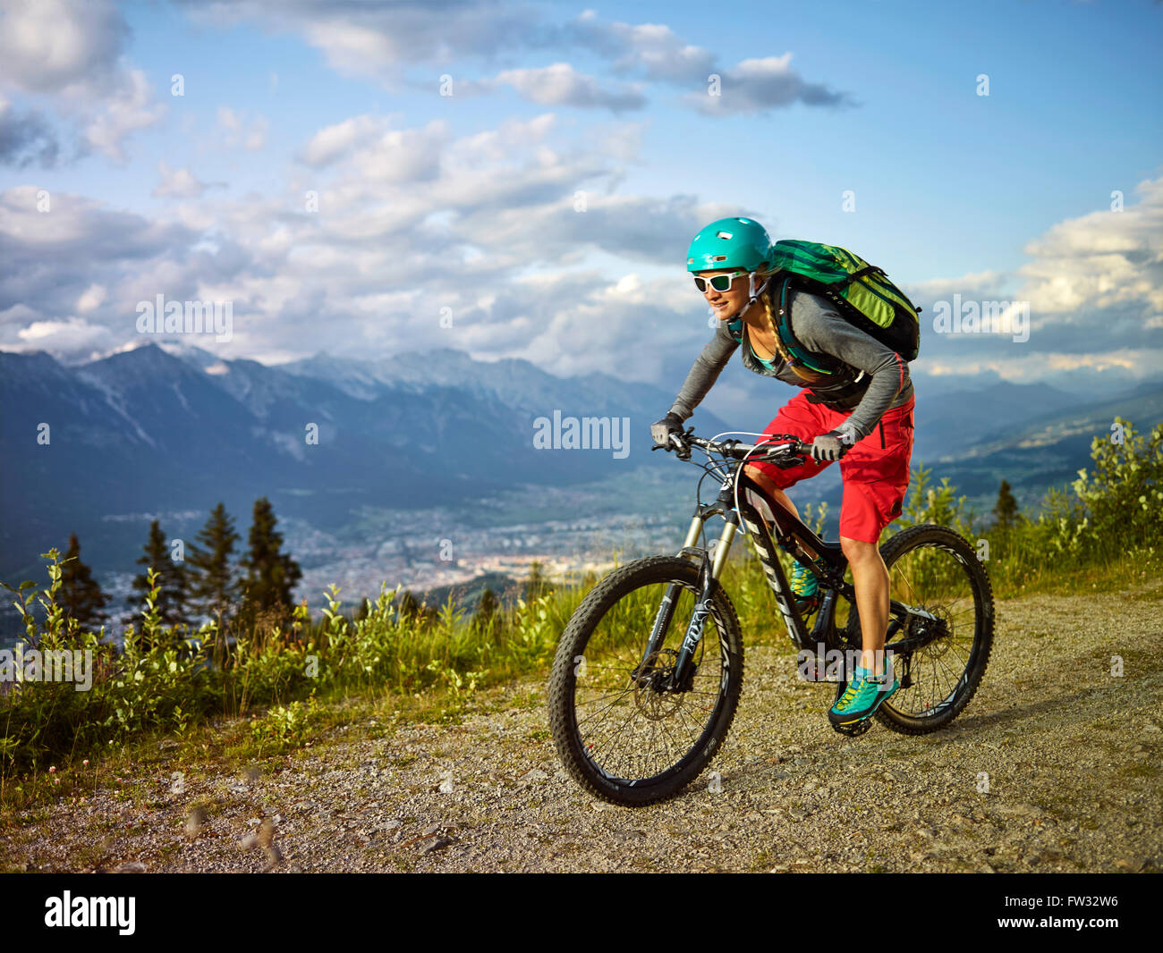 Mountain biker con un casco a cavallo su una strada di ghiaia, Mutterer Alm vicino a Innsbruck, catena settentrionale delle Alpi dietro il Tirolo Foto Stock