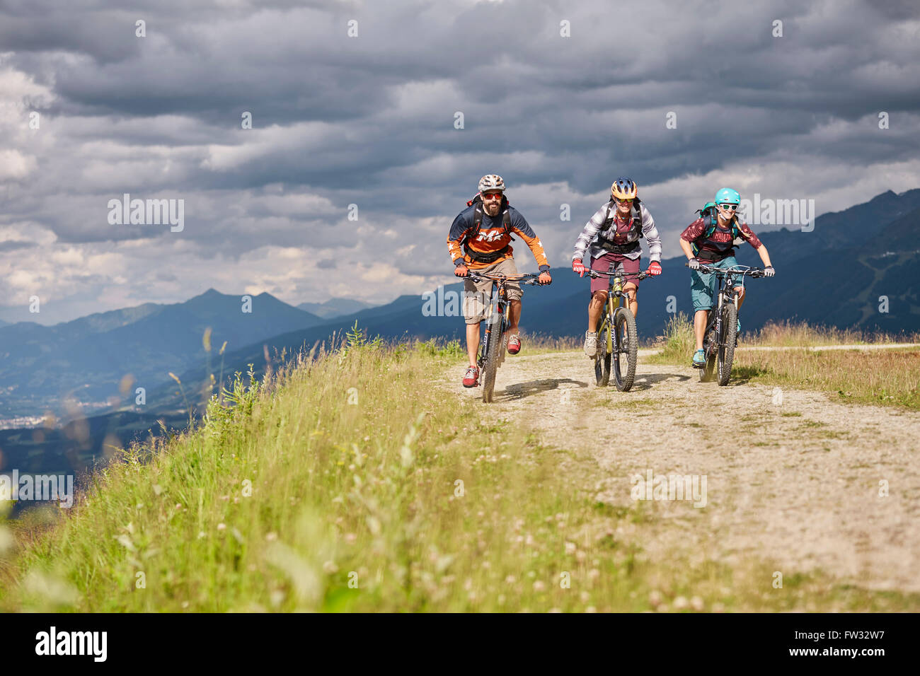Tre i ciclisti di montagna con i caschi a cavallo su una strada di ghiaia, Mutterer Alm vicino a Innsbruck in Tirolo, Austria Foto Stock