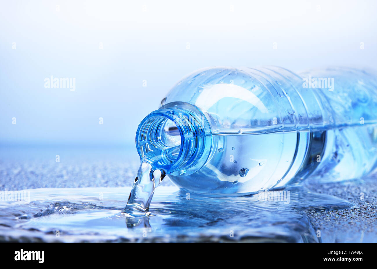Versare acqua dalla bottiglia di plastica con la riflessione su bianco e lo sfondo blu Foto Stock
