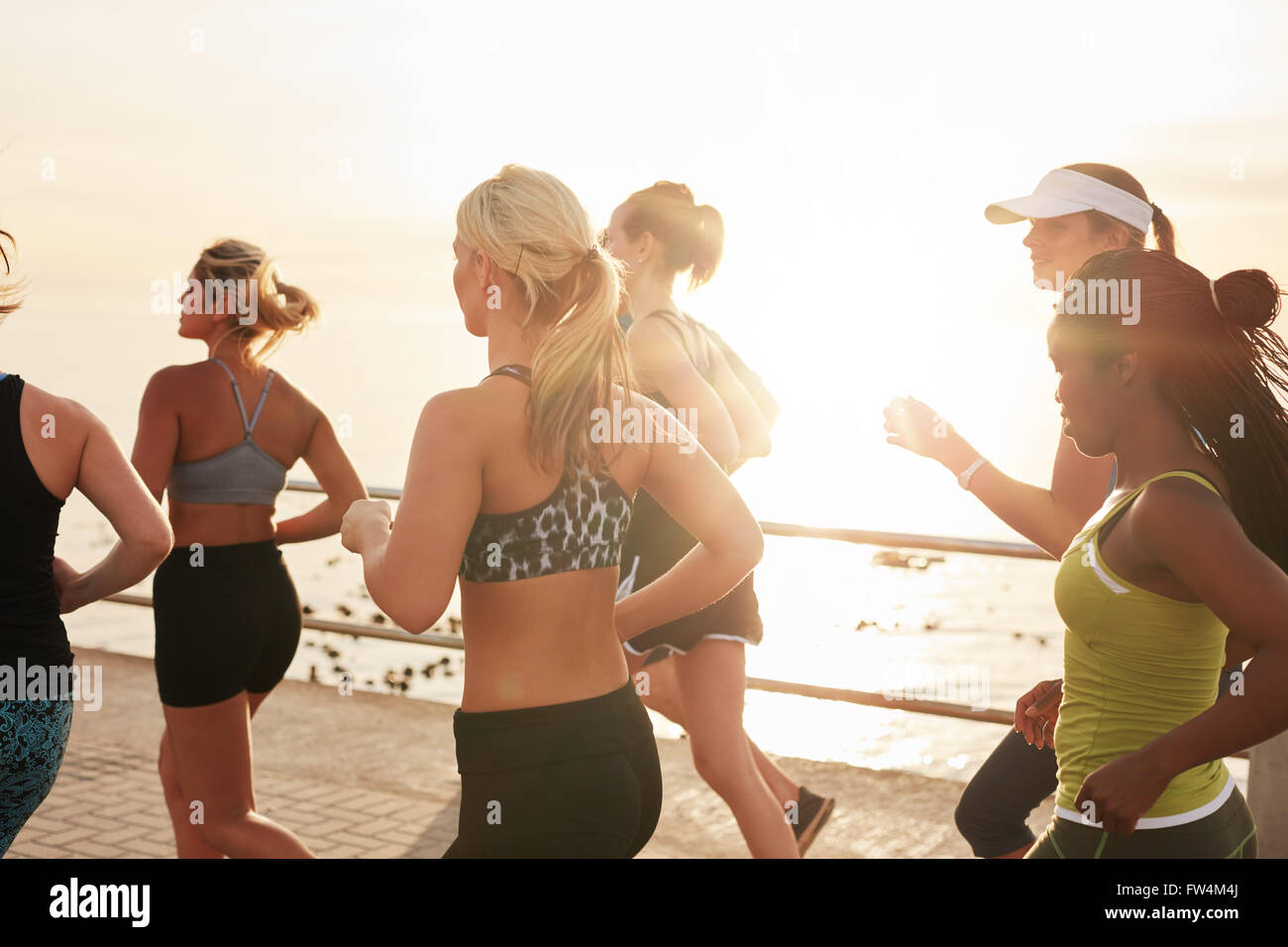 Inquadratura di gruppo di montare le giovani donne in esecuzione insieme sulla strada sul mare al tramonto. Multi etnico gruppo di donne che svolgono in esecuzione traini Foto Stock