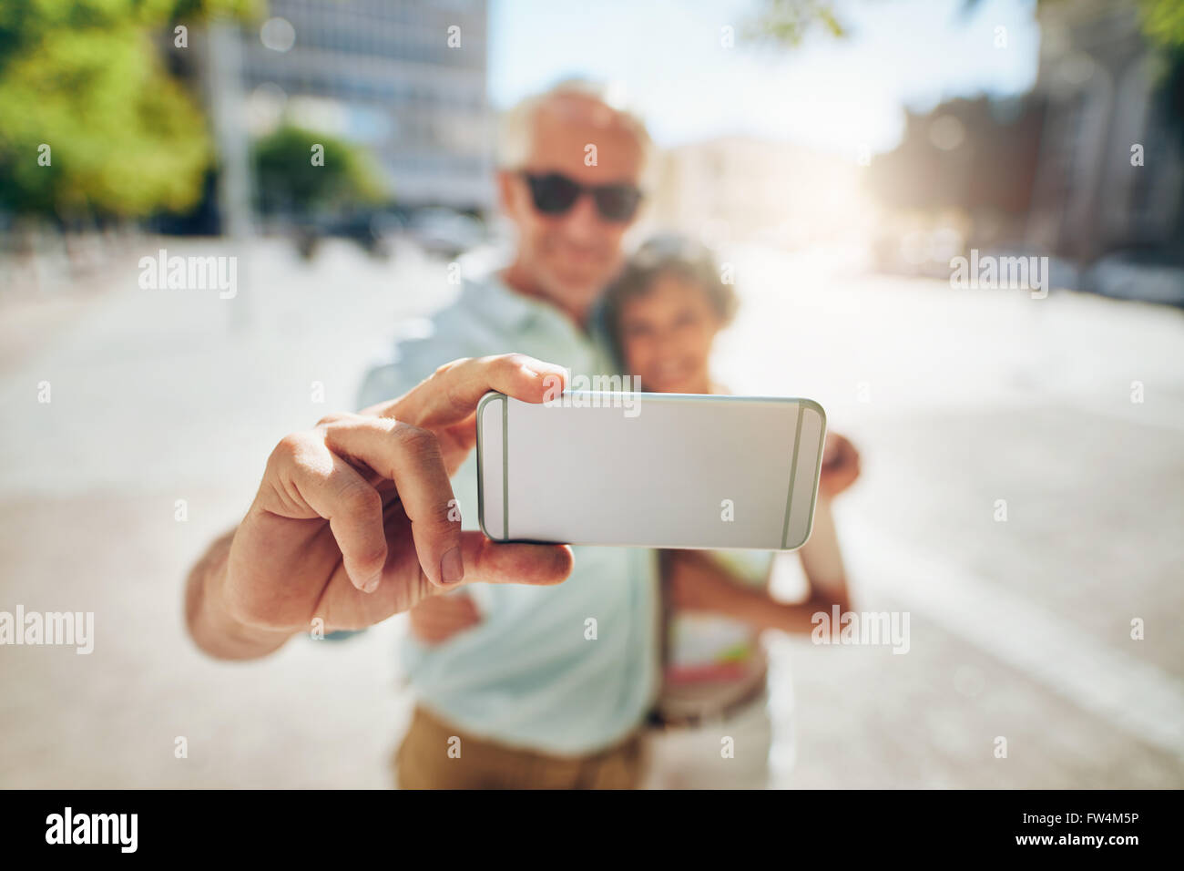 Felice coppia senior abbracciando e prendendo un autoritratto su telefono cellulare all'esterno. Turistica prendendo selfie, concentrarsi sul telefono cellulare. Foto Stock