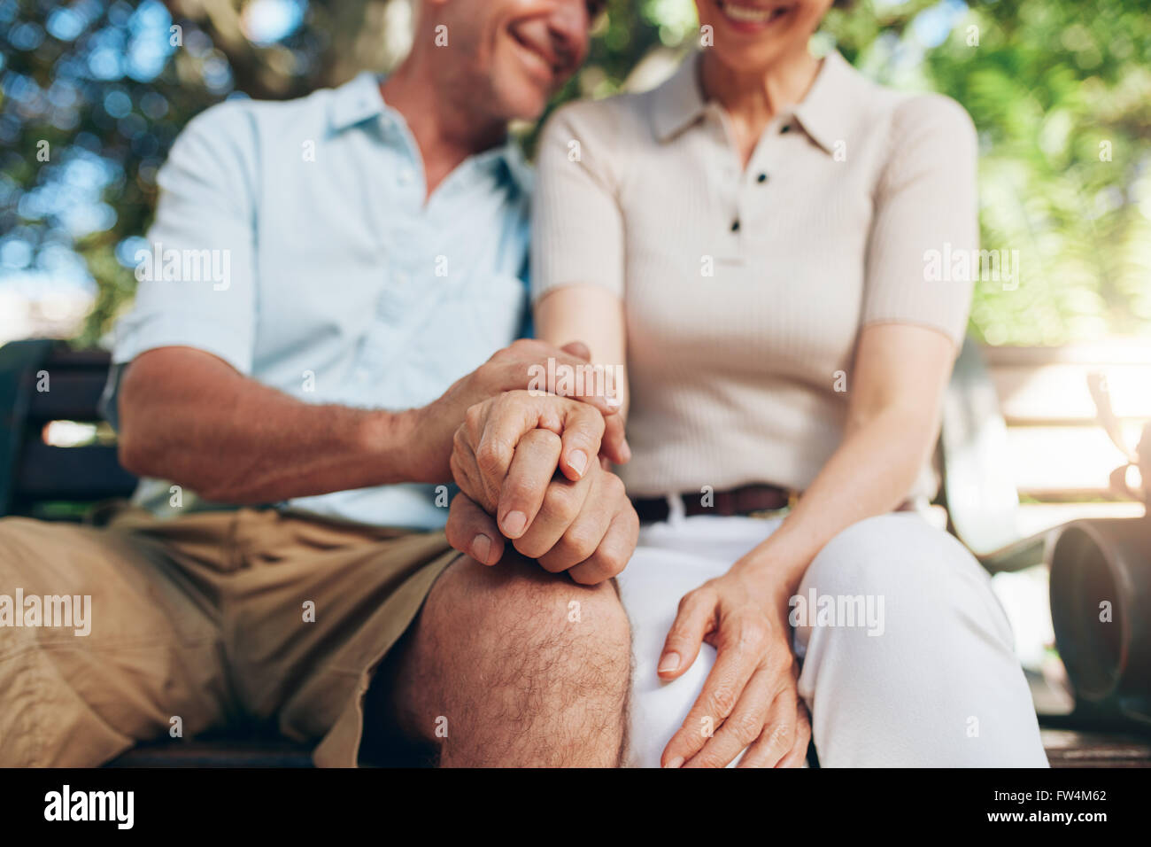 Amorevole coppia senior seduti insieme e tenendo le mani in un parco. Chiudere l'immagine con focus sulle mani. Foto Stock