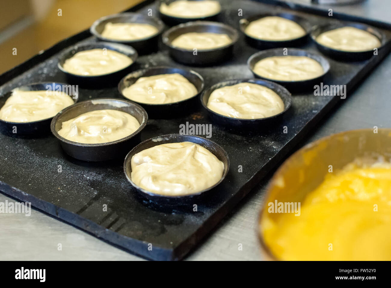 La preparazione di muffin per il forno in un forno a crudo con impasto aromatizzato disposti in singole teglie su un vassoio di metallo Foto Stock