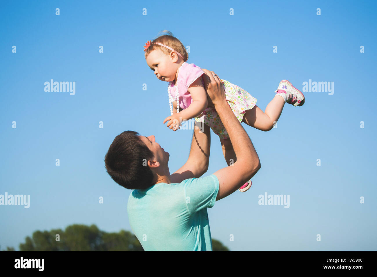 Bambina in abito rosa sulle mani di suo padre. Felice bambina godendo giochi attivi con il suo papà. Foto Stock