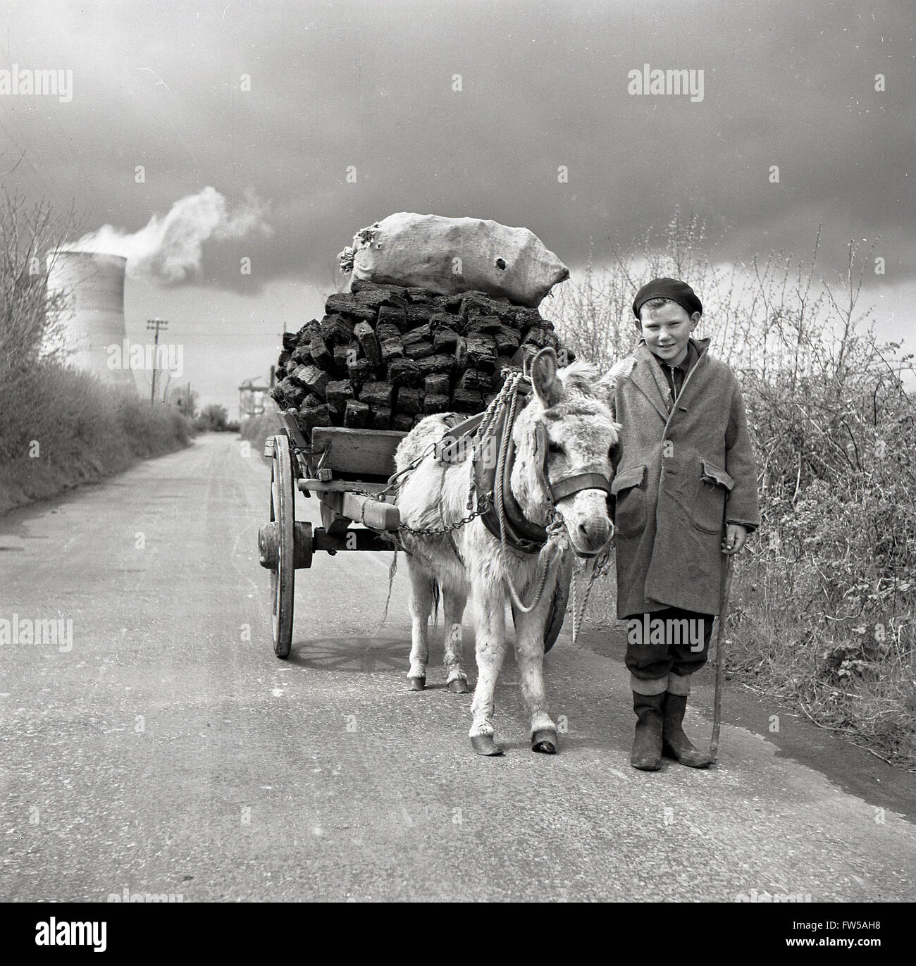 1950, quadro storico di J Allan Cash, di un giovane ragazzo irlandese con un pony e carretto caricato con torba su una corsia di campagna nella zona rurale occidentale dell'Irlanda. La torba o il tappeto erboso è stato raccolto dalle paludi in Irlanda per secoli per essere utilizzato come combustibile per il riscaldamento invernale. Foto Stock