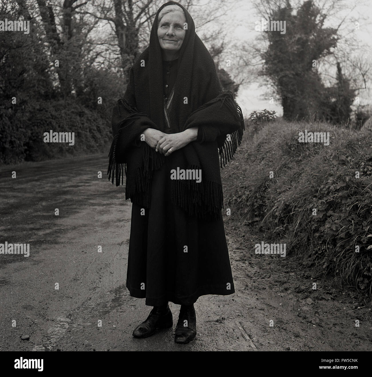 Anni Cinquanta storiche, signora anziana in nero con scialle sorge accanto  a una strada bagnata in Irlanda rurale prima di frequentare la Messa Foto  stock - Alamy