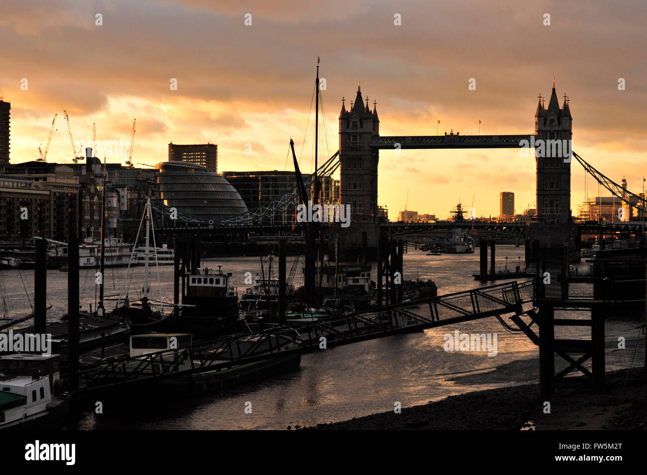 A montanti e armamento di spedizioni presso il St Katharine Dock, da Wapping, Londra, con il Tower Bridge al tramonto, l'inverno. Iniziato 1823; i magazzini intorno a questo dock sono state costruite vicino all'acqua, in modo che le merci possano essere scaricati mediante gru direttamente dalla nave in magazzino. Questo taglio verso il basso il rischio di furto e così il dock è stato usato per carichi utili come avorio, spezie e marmo, ecc. Charles Dickens, romanziere inglese, ha avuto una durata del collegamento a Wapping e Limehouse, impostazione numerose scene dal fiume, compresi Quilp's Yard nel vecchio negozio di curiosità e capitano Cuttle della casa di Domb Foto Stock