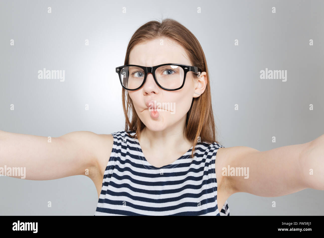 Funny carina ragazza adolescente in bicchieri rendere divertente la faccia e prendendo selfie Foto Stock