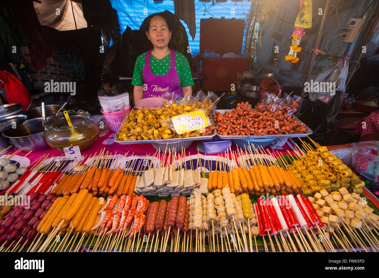 Donna al mercato in stallo con vari spiedini di carne e pesce e salsiccia, stallo alimentari, alimenti per la vendita su un mercato notturno, Thailandia Foto Stock
