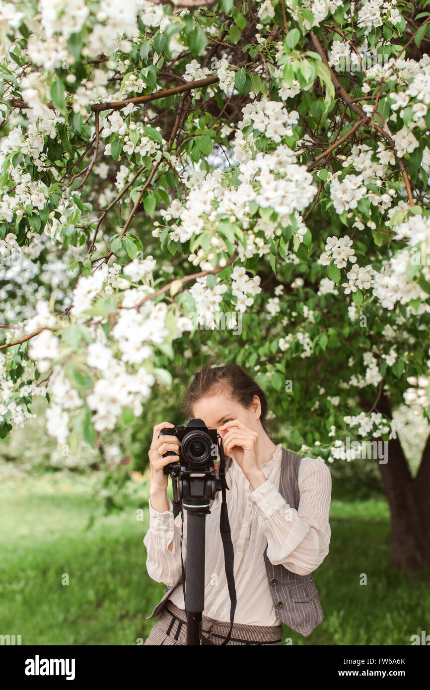 Donna spara a la fotocamera su un cavalletto monopiede contro uno sfondo di alberi, parco, Apple Blossom Foto Stock