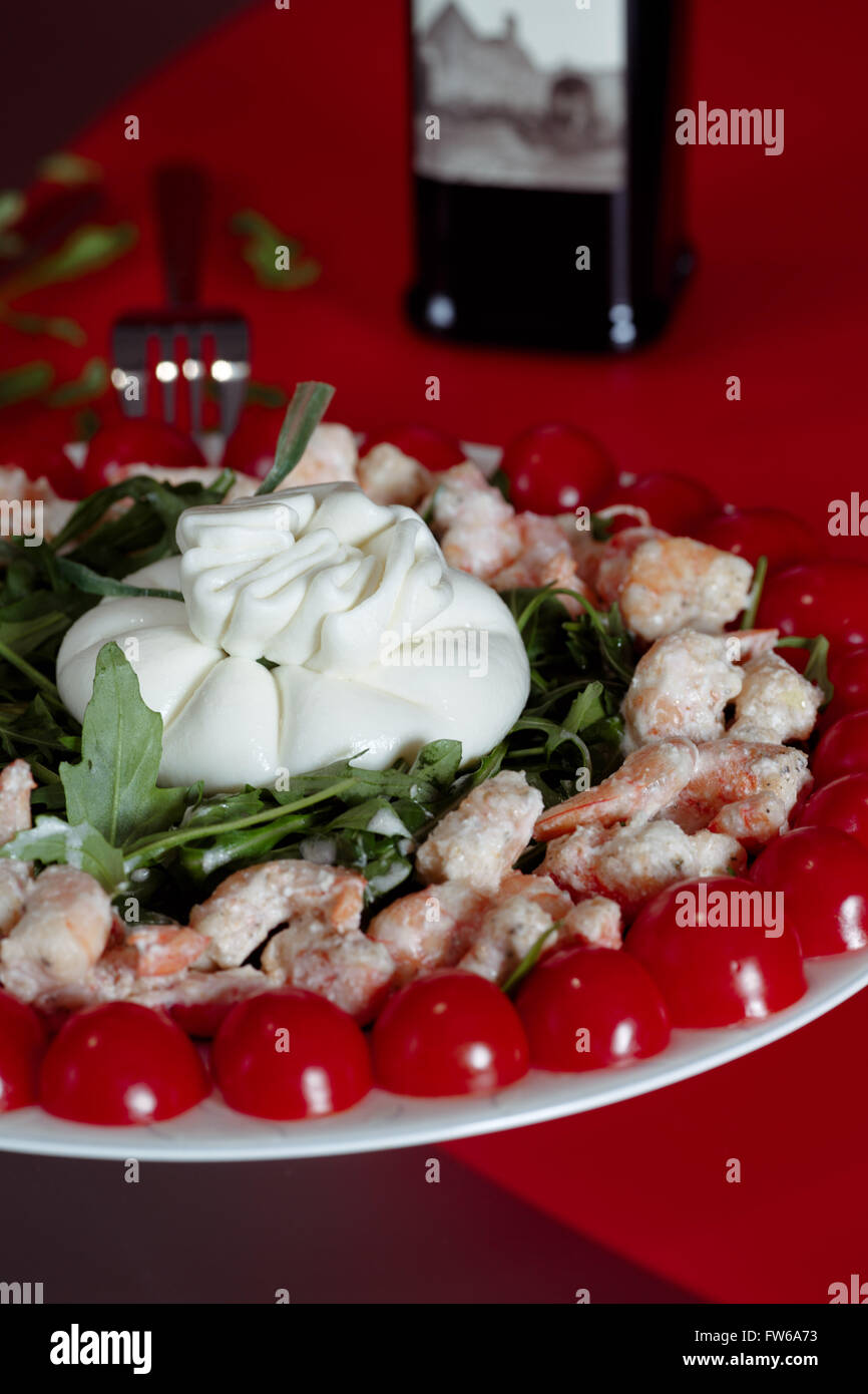Insalata formaggio Buratti, gamberetti, rucola, pomodorini con olio d'oliva, servita su uno sfondo rosso con una forcella, close-up Foto Stock