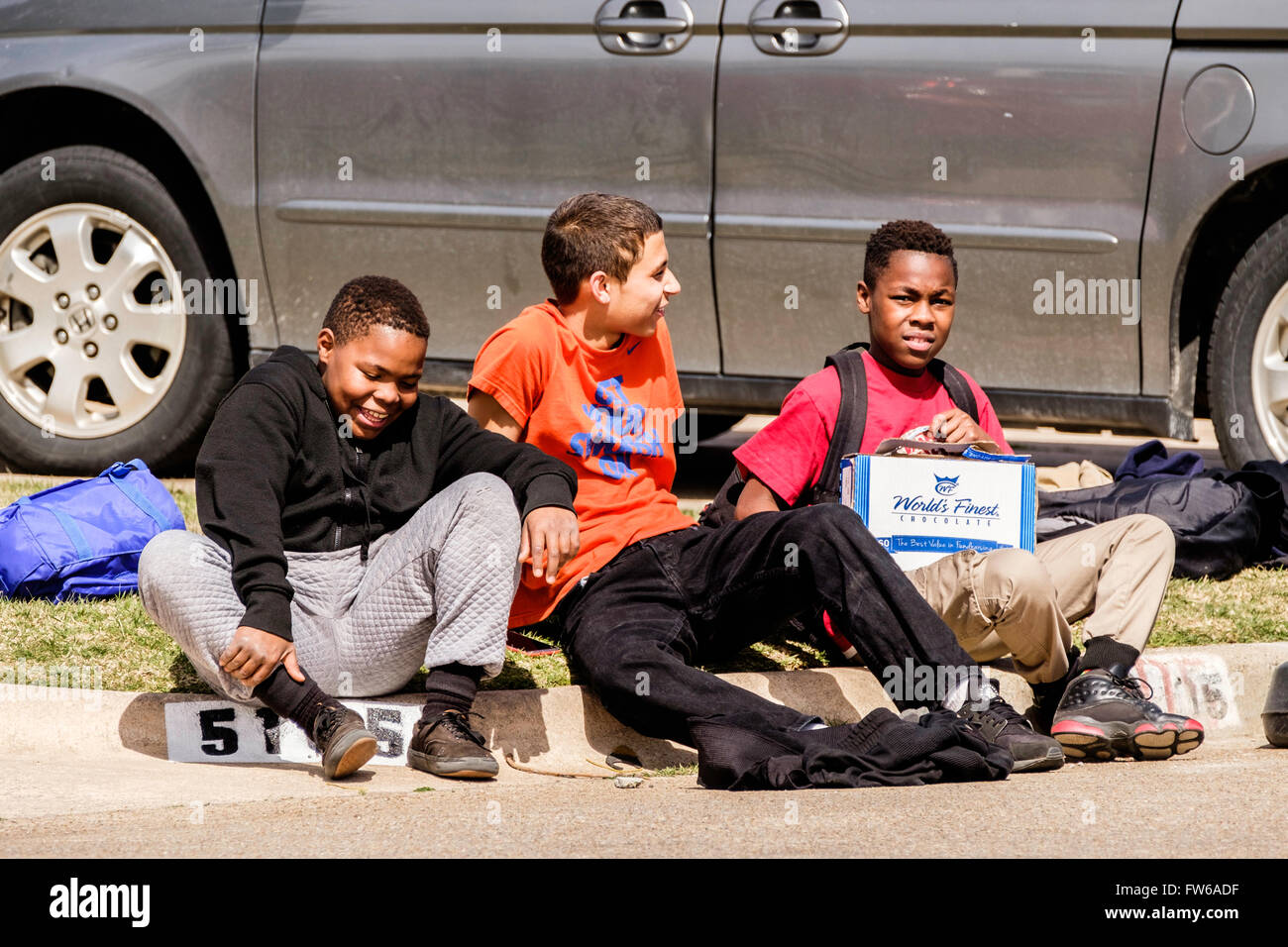 Tre ridendo preteen boys sedersi su un cordolo di vicinato insieme nella città di Oklahoma, Oklahoma, Stati Uniti d'America. Americano africano, ispanica. Foto Stock