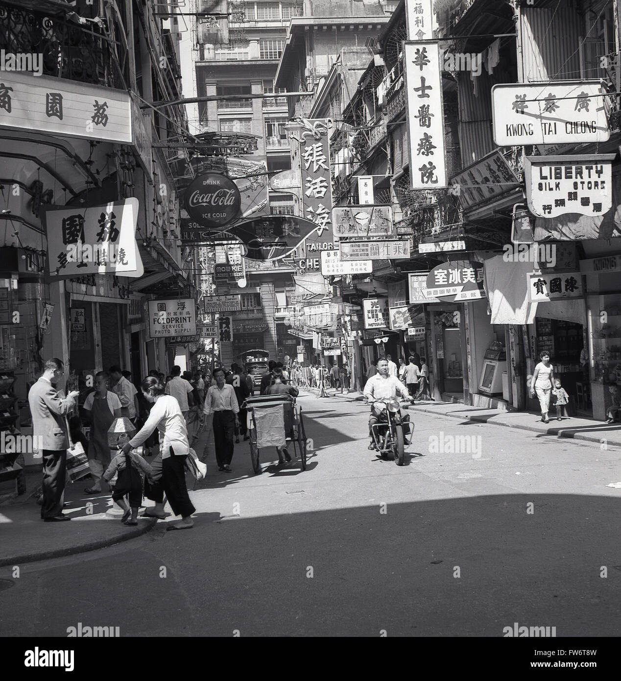 Anni '50, storico, angolo di strada, città vecchia, Hong Kong, Mostra gli edifici, cartellonistica in cinese, inglese e gente locale. Anche nel trasporto di immagini dell'epoca, un risciò e un uomo locale su una moto. Foto Stock