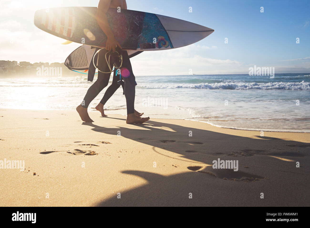Australian surfers ragazzi a piedi lungo la spiaggia di Bondi con tavole da surf e sun flare Foto Stock