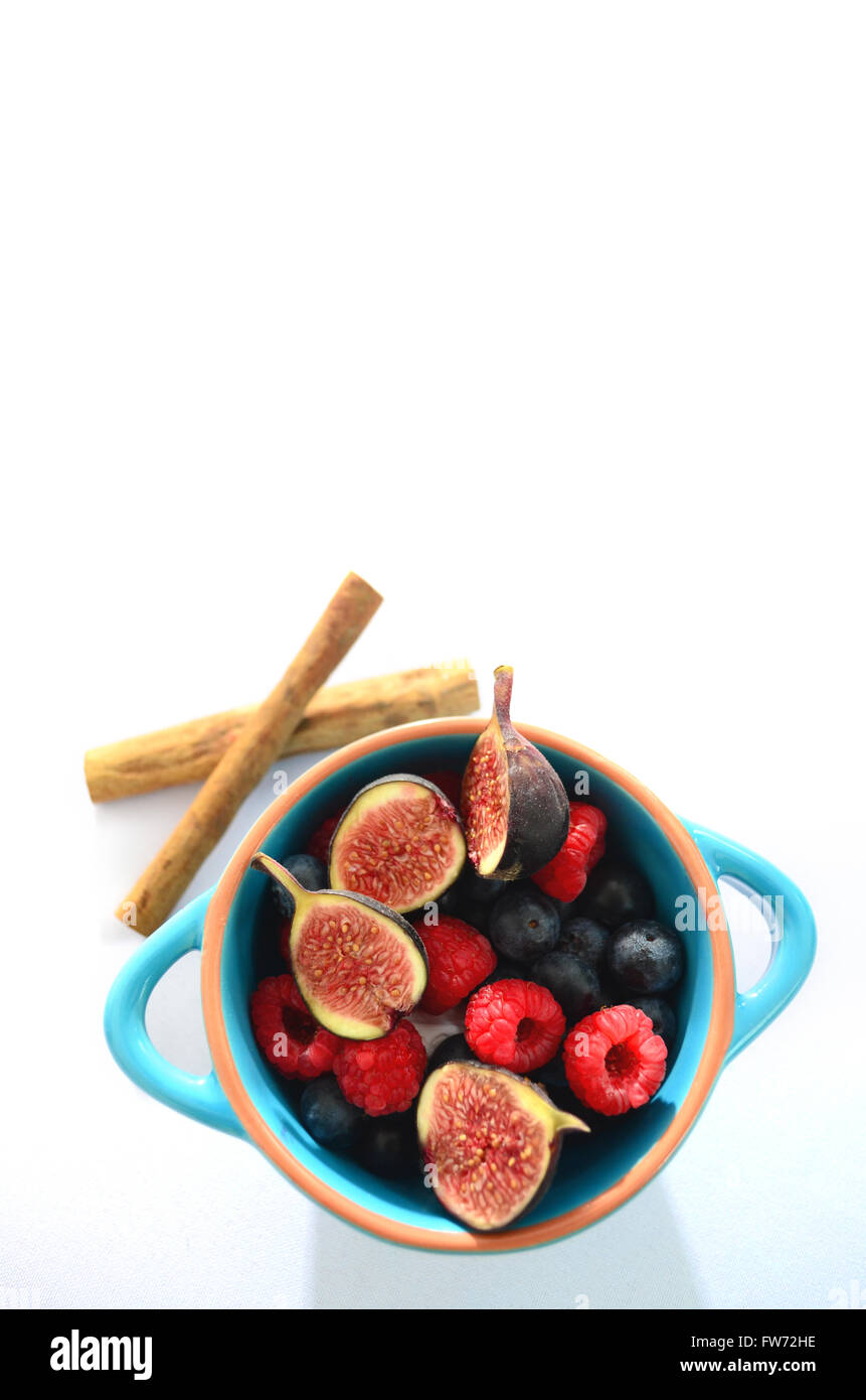 Colazione blu ciotola di frutti di bosco freschi, fichi, cannella o cassia bastoni con copia spazio. Foto Stock