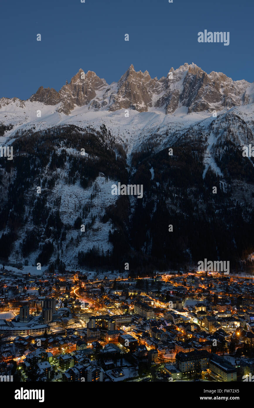 Resort di montagna di notte dominato da alte cime frastagliate. Aguilles (Needles) de Chamonix, Haute-Savoie, Auvergne-Rhône-Alpes, Francia. Foto Stock