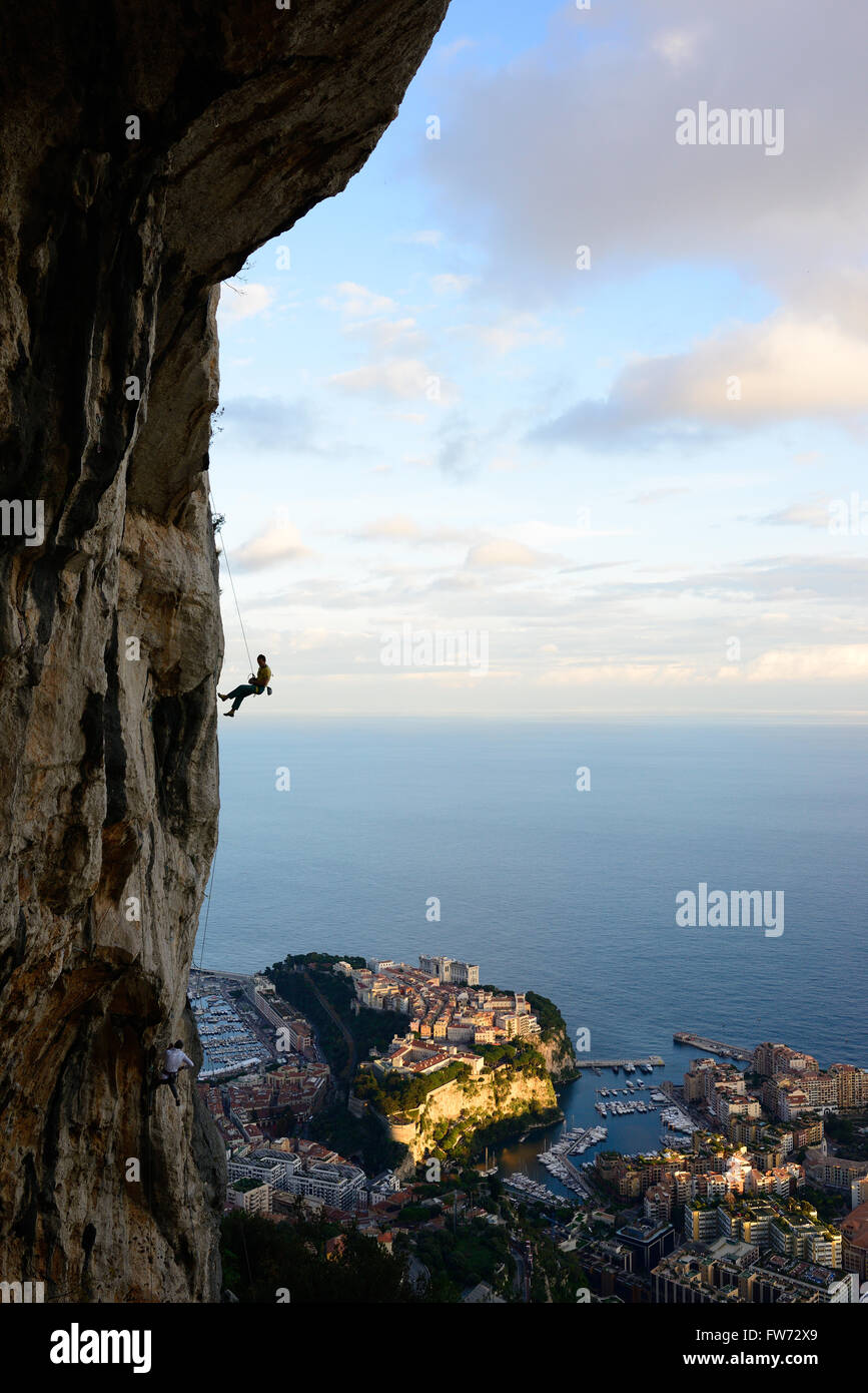 Uomo che abseiling una scogliera calcarea con Monaco e il Mar Mediterraneo per sfondo. La Turbie, Alpes-Maritimes, Costa Azzurra, Francia. Foto Stock