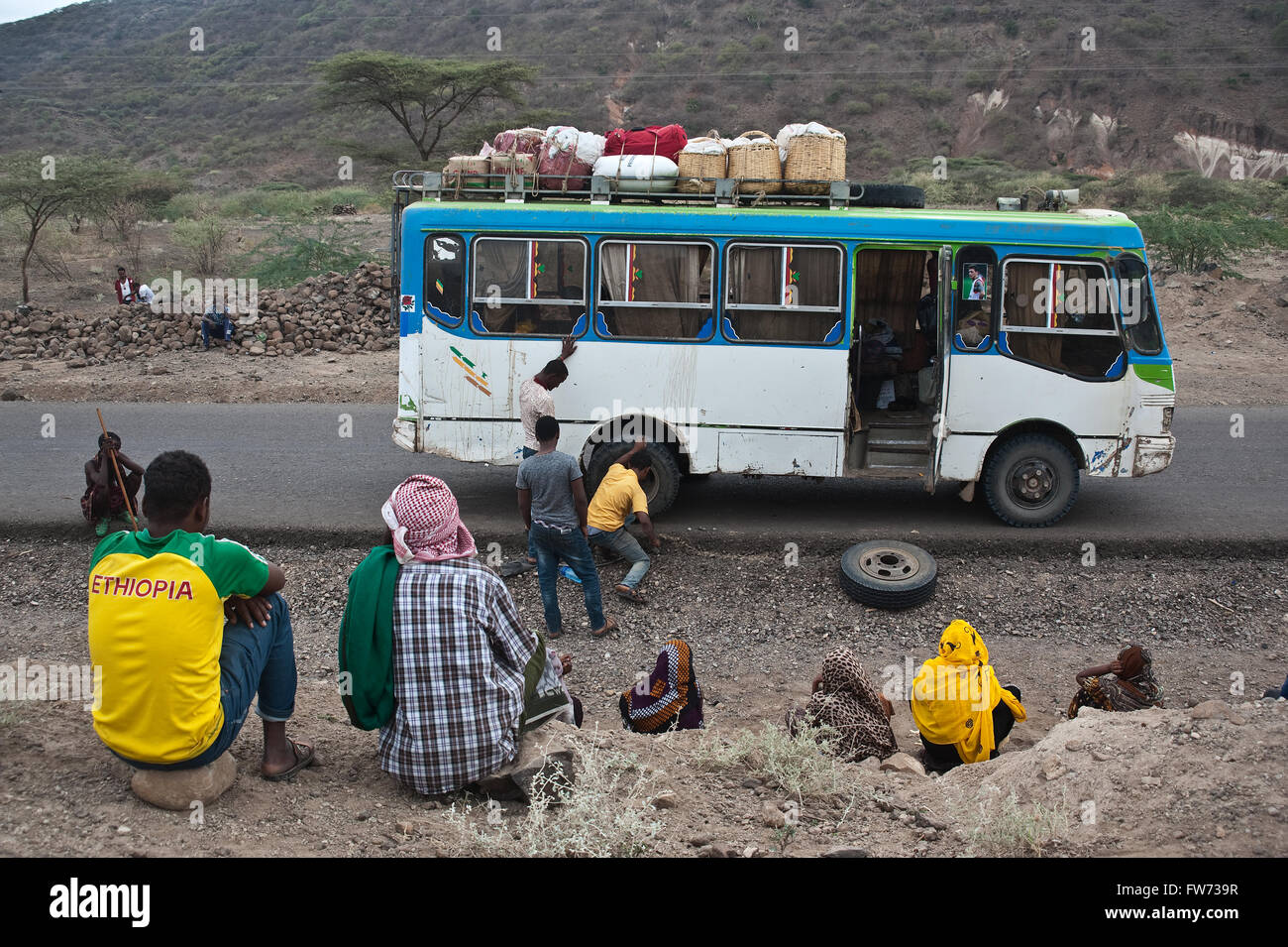 Un bus privato dipendente è di cambiare il pneumatico sgonfio del bus lavora nel mentre i passeggeri sono a guardare lui ( Etiopia) Foto Stock