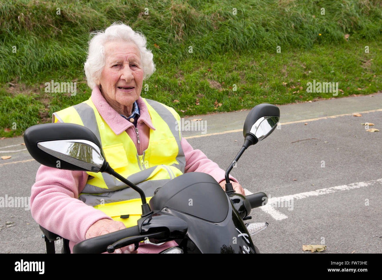 Ritratto di una donna anziana seduto nel suo scooter di mobilità che indossa un giallo hi-vis giubbotto di sicurezza Foto Stock