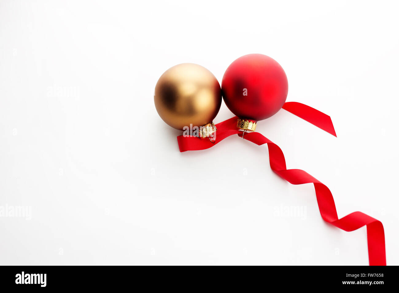 Uno rosso e uno di vetro dorato ornamento di Natale con nastro rosso su sfondo bianco. Foto Stock