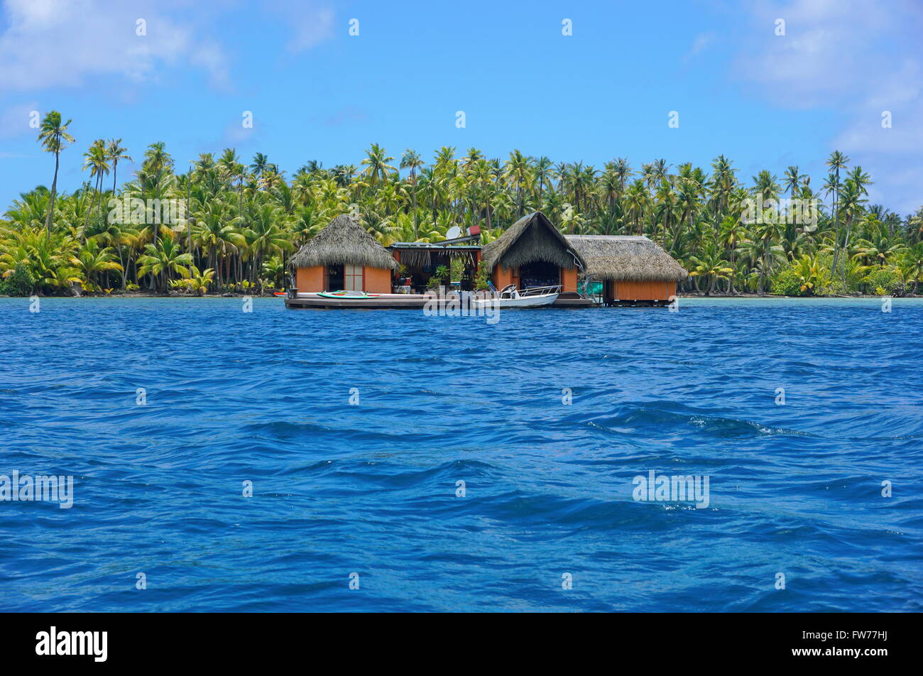 Home esotici con tetto di paglia sopra l'acqua e una piantagione di palme di cocco in background, Huahine, Polinesia Francese Foto Stock