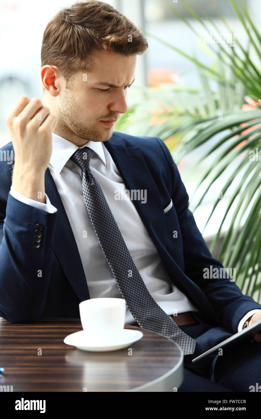 Ritratto di bello uomo di successo bere il caffè e guardare alla tavoletta digitale schermo seduto in coffee shop Foto Stock