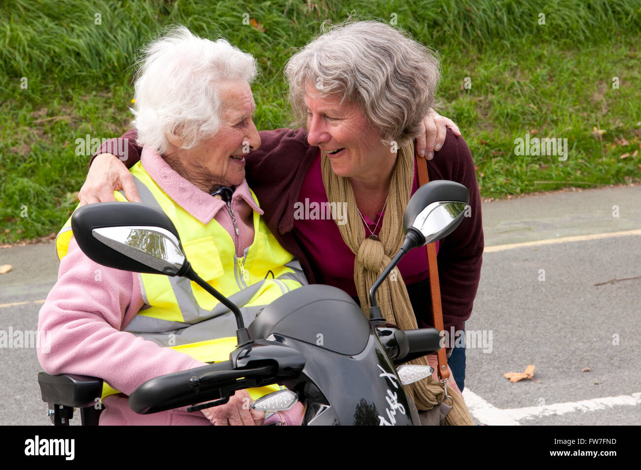 Donna anziana seduto nel suo scooter di mobilità a parlare con il suo caregiver Foto Stock