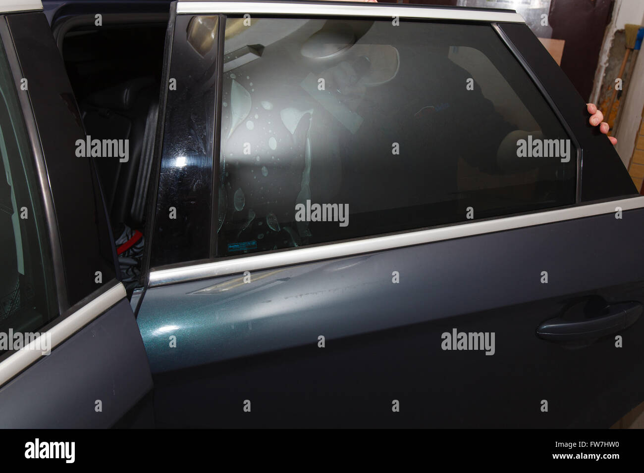 Applicazione di lamina di colorazione sul finestrino di un'automobile in un garage Foto Stock