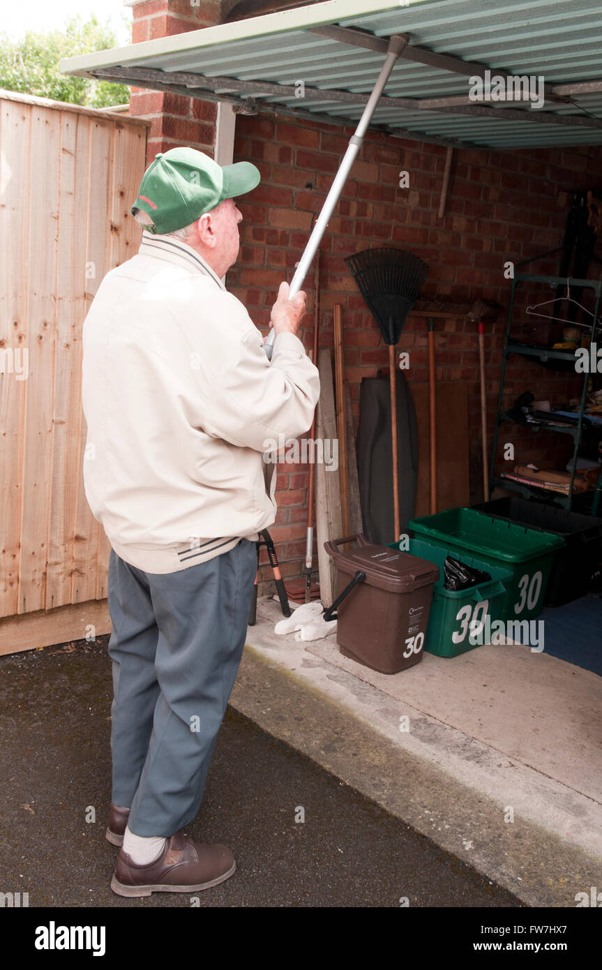 Vista posteriore di un uomo anziano con il suo bastone per spingere la sua porta di garage fino Foto Stock