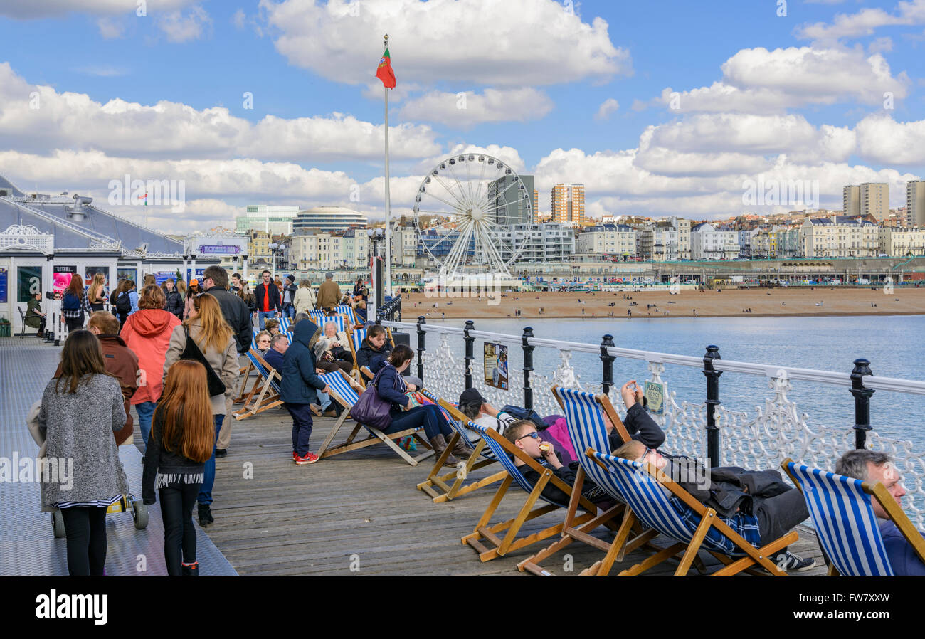 La gente camminare e seduti in sedie a sdraio sul molo di Brighton a Brighton, Brighton & Hove, East Sussex, Inghilterra, Regno Unito. Foto Stock