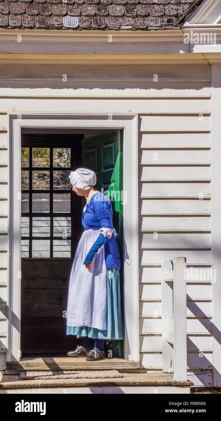 Donna senior di Colonial Williamsburg in inglese tradizionale abito blu in piedi nella porta Foto Stock