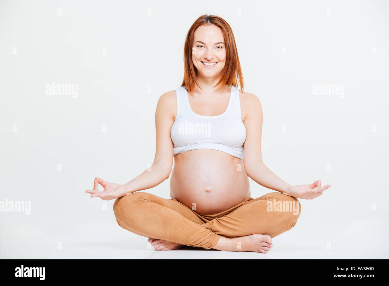 Sorridente donna incinta meditando isolato su uno sfondo bianco Foto Stock