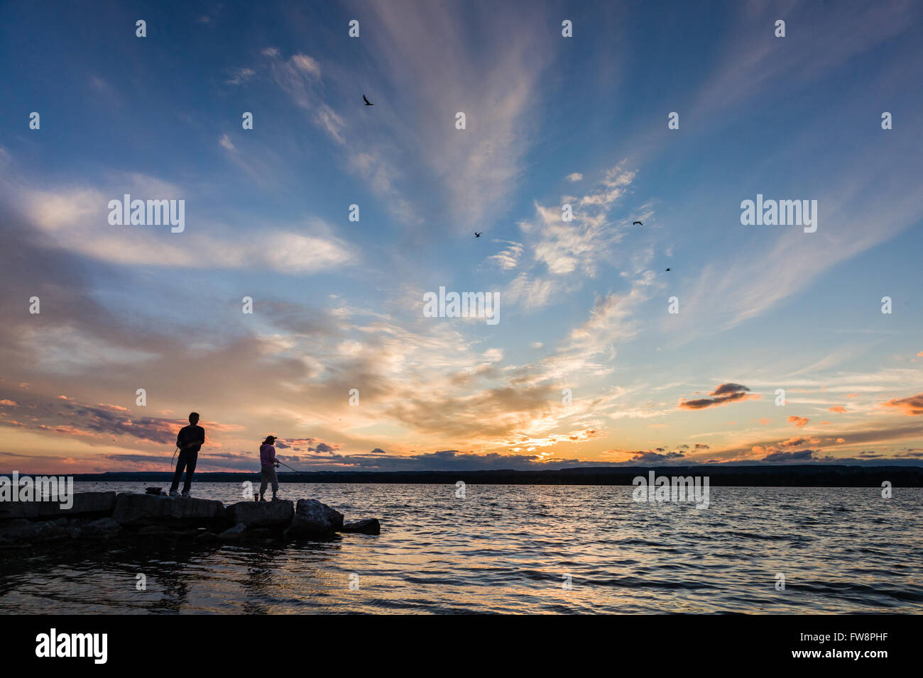 Una scena del tramonto sulla baia di Burlington con due piccole sagome di persone di pesca. Foto Stock