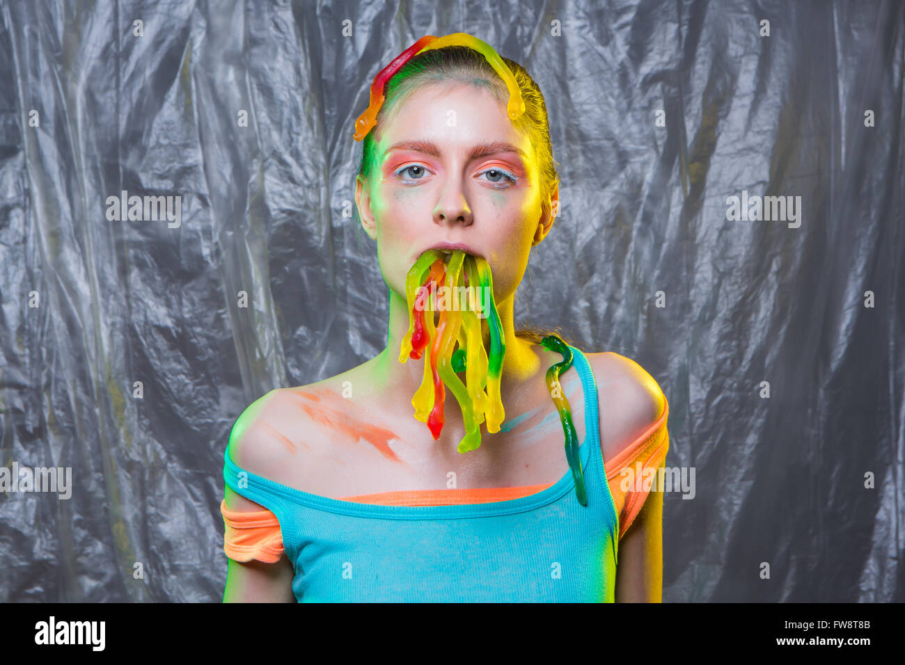 Giovane donna con colorate compongono contiene gelatina gommoso worm caramelle in bocca. Foto Stock