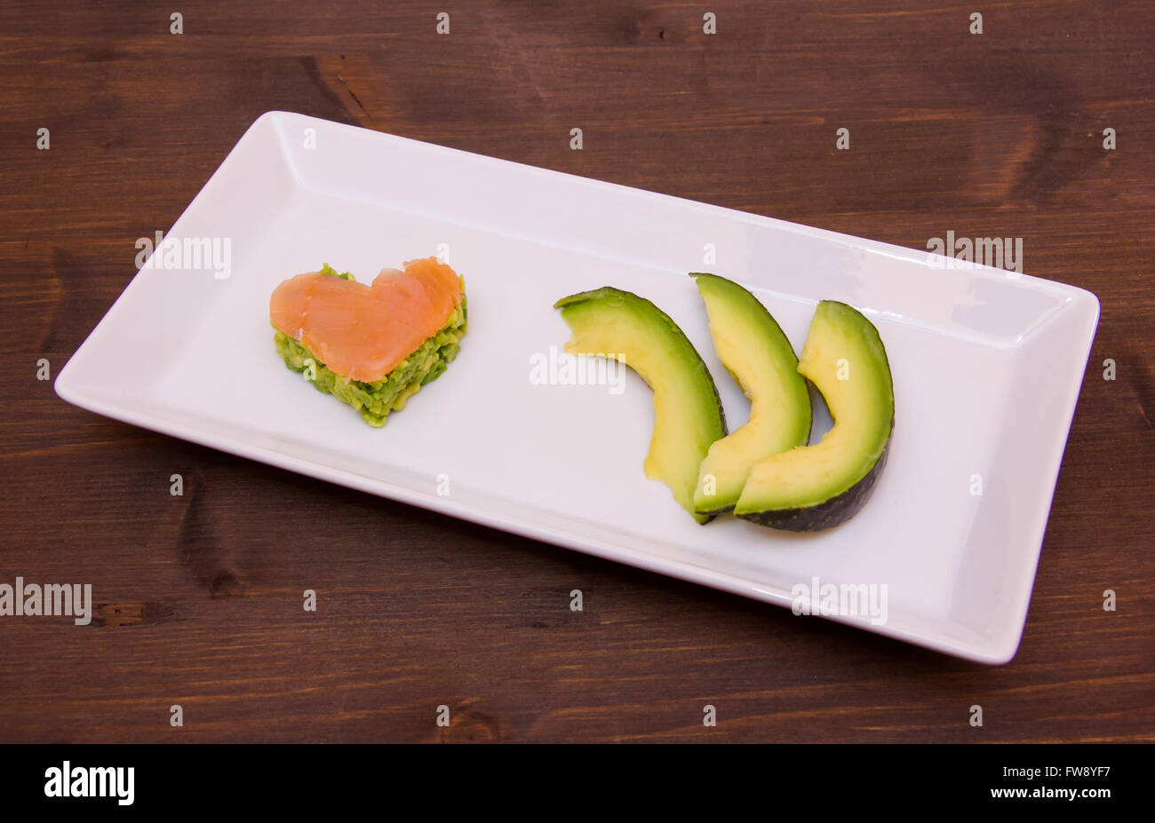 Fette di avocado e di avocado e salmone affumicato a forma di cuore sul vassoio su legno Foto Stock
