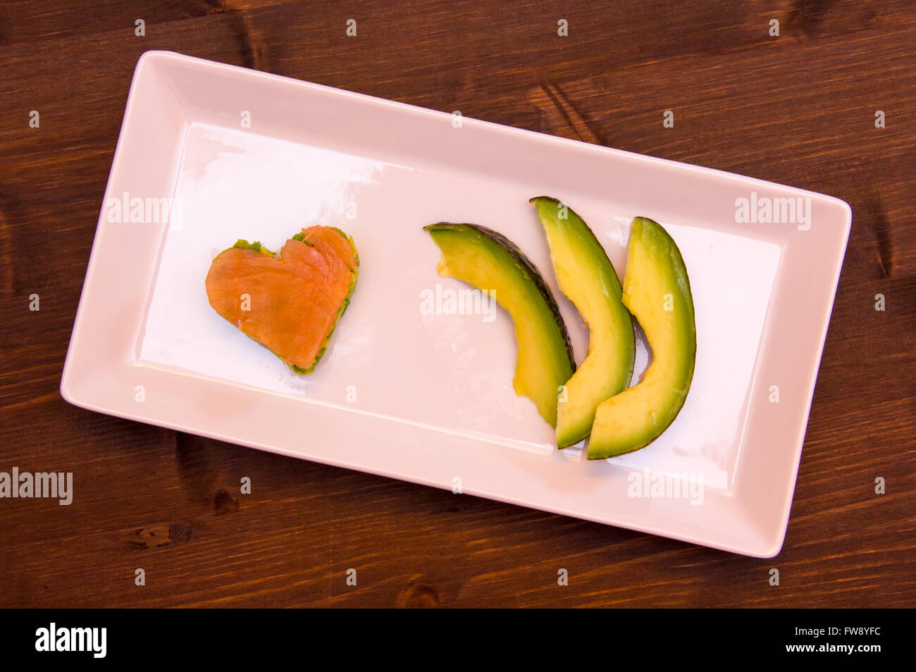 Fette di avocado e di avocado e salmone affumicato in una forma di cuore sul vassoio su legno visto da sopra Foto Stock