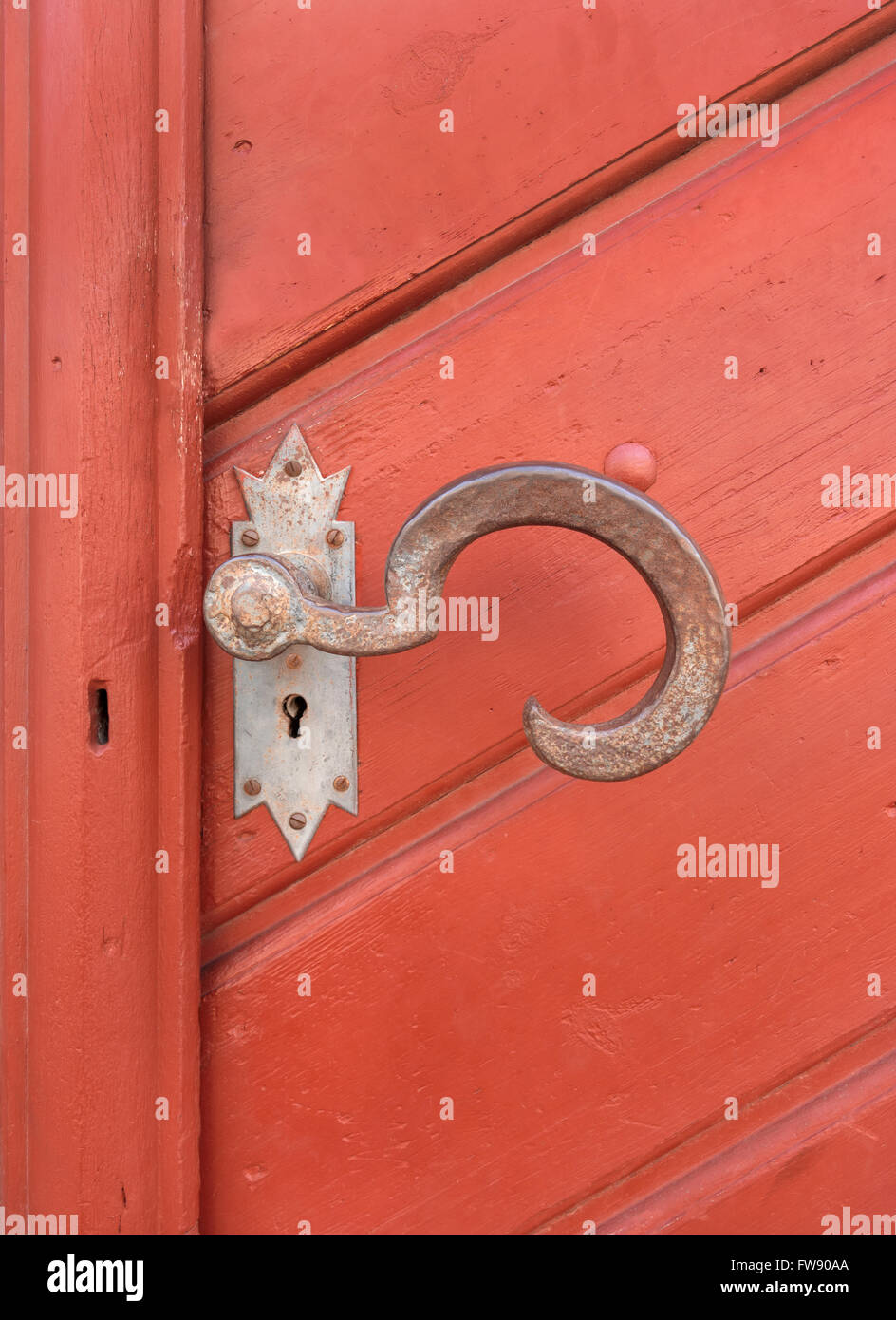 Vecchio, grande, artisticamente curvo maniglia della porta di metallo arrugginito su un marrone rossiccio e porta in legno Foto Stock