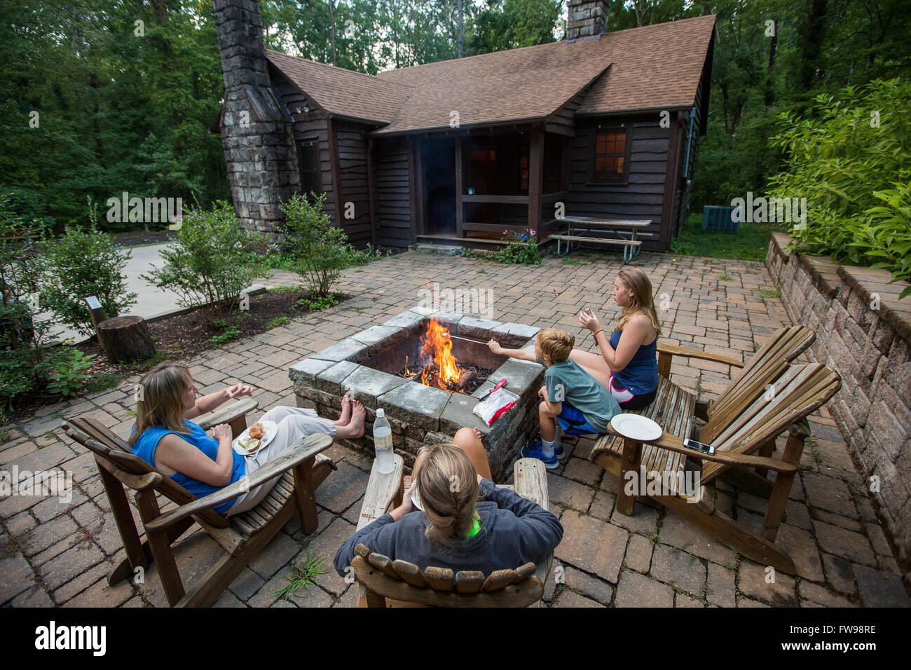 Famiglia di mangiare intorno a una buca per il fuoco alla cabina su Table Rock State Park nel Sud Carolina. Foto Stock