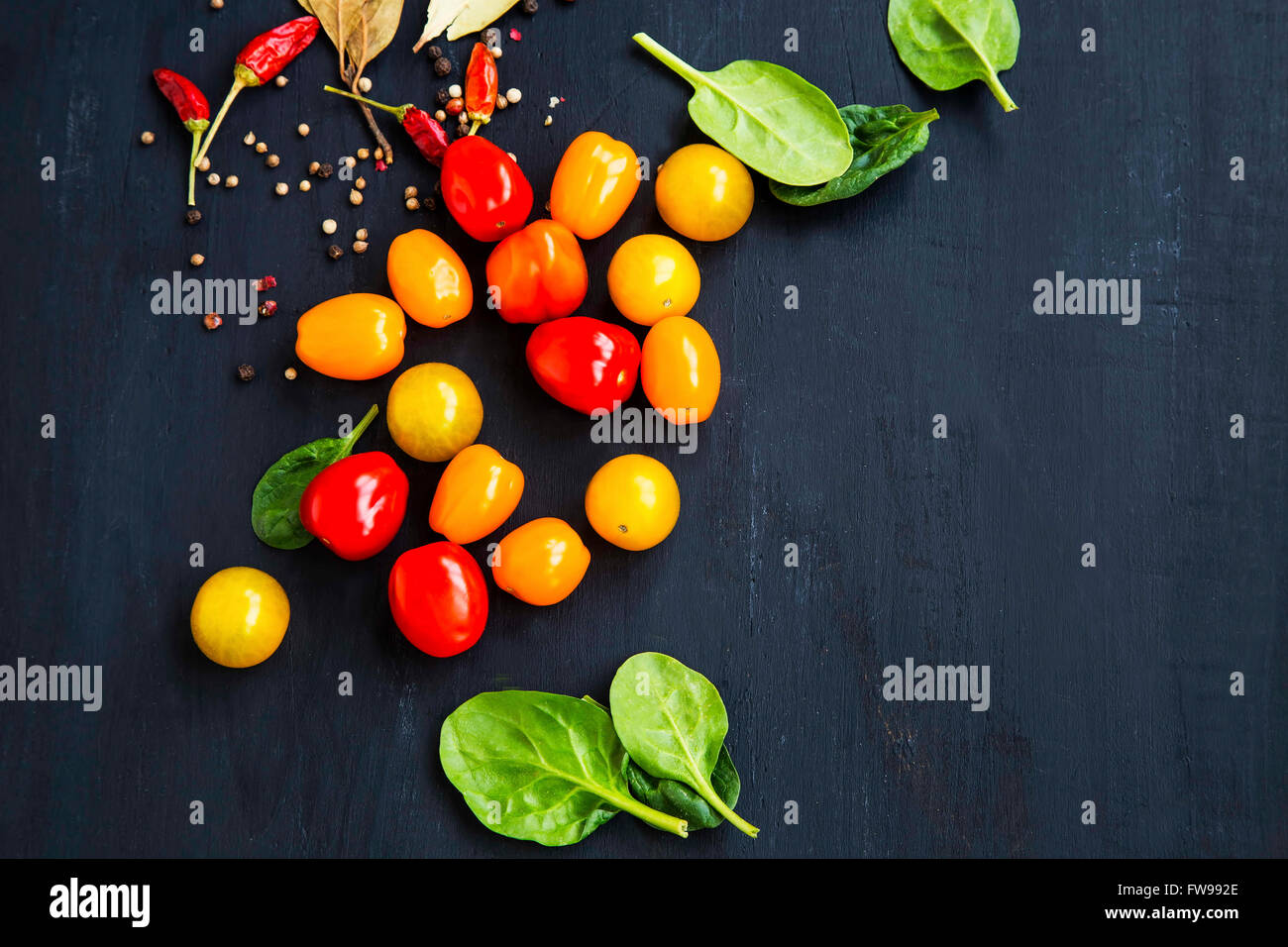 Il giallo e il rosso dei pomodori ciliegia con foglie di spinaci e spezie su sfondo di legno Foto Stock