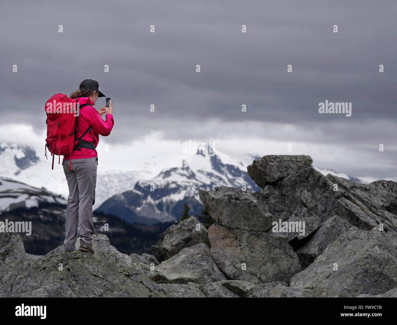 Una giovane donna escursionista sul vertice di montagna tenendo un telefono intelligente in Whistler Blackcomb escursione alpina, BC, Canada Foto Stock