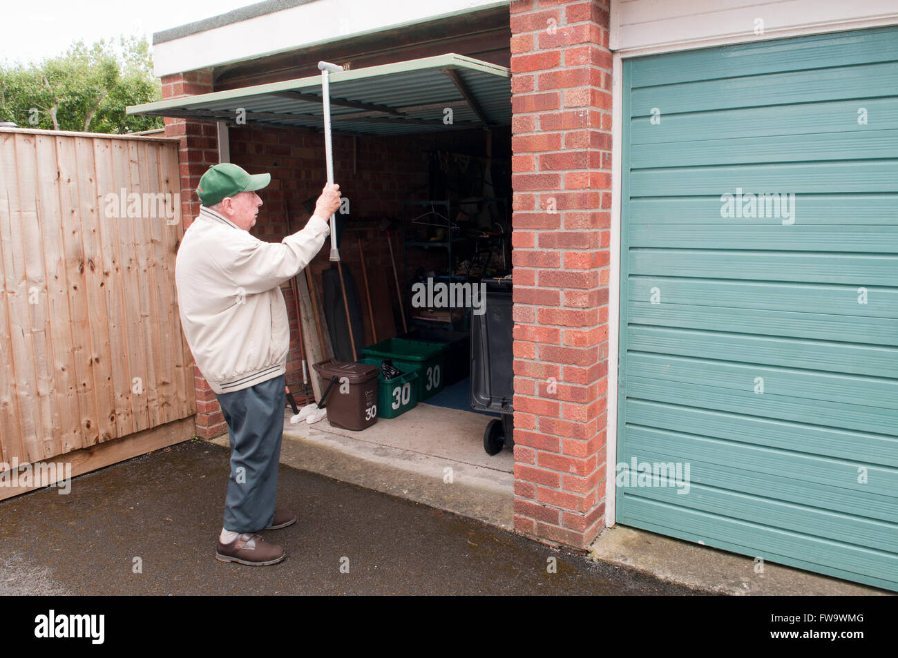 Vista posteriore di un uomo anziano con il suo bastone per tirare il suo porta del garage verso il basso Foto Stock