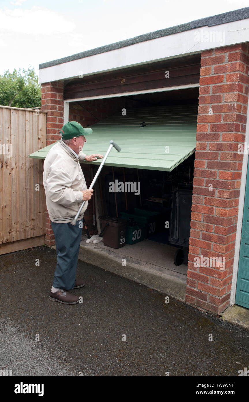 Vista posteriore di un uomo anziano con il suo bastone per tirare il suo porta del garage verso il basso Foto Stock