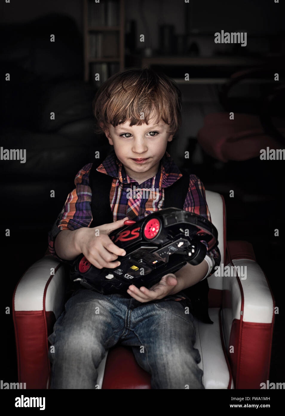 Un ragazzo seduto in poltrona tenendo un auto giocattolo in dark room Foto Stock