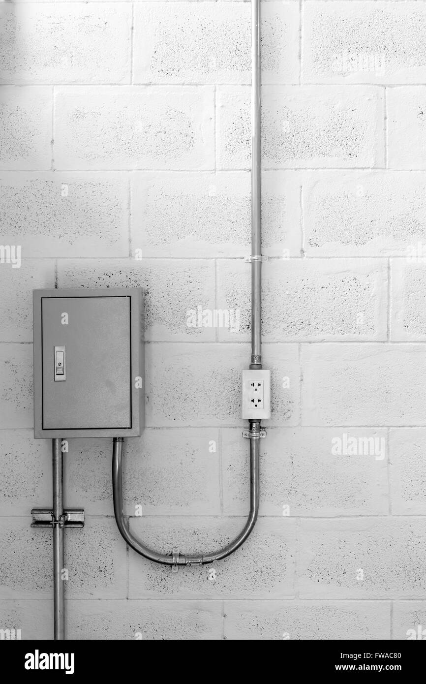 Cassetta elettrica sulla parete di cemento con il tubo in acciaio e il tappo, in bianco e nero Foto Stock