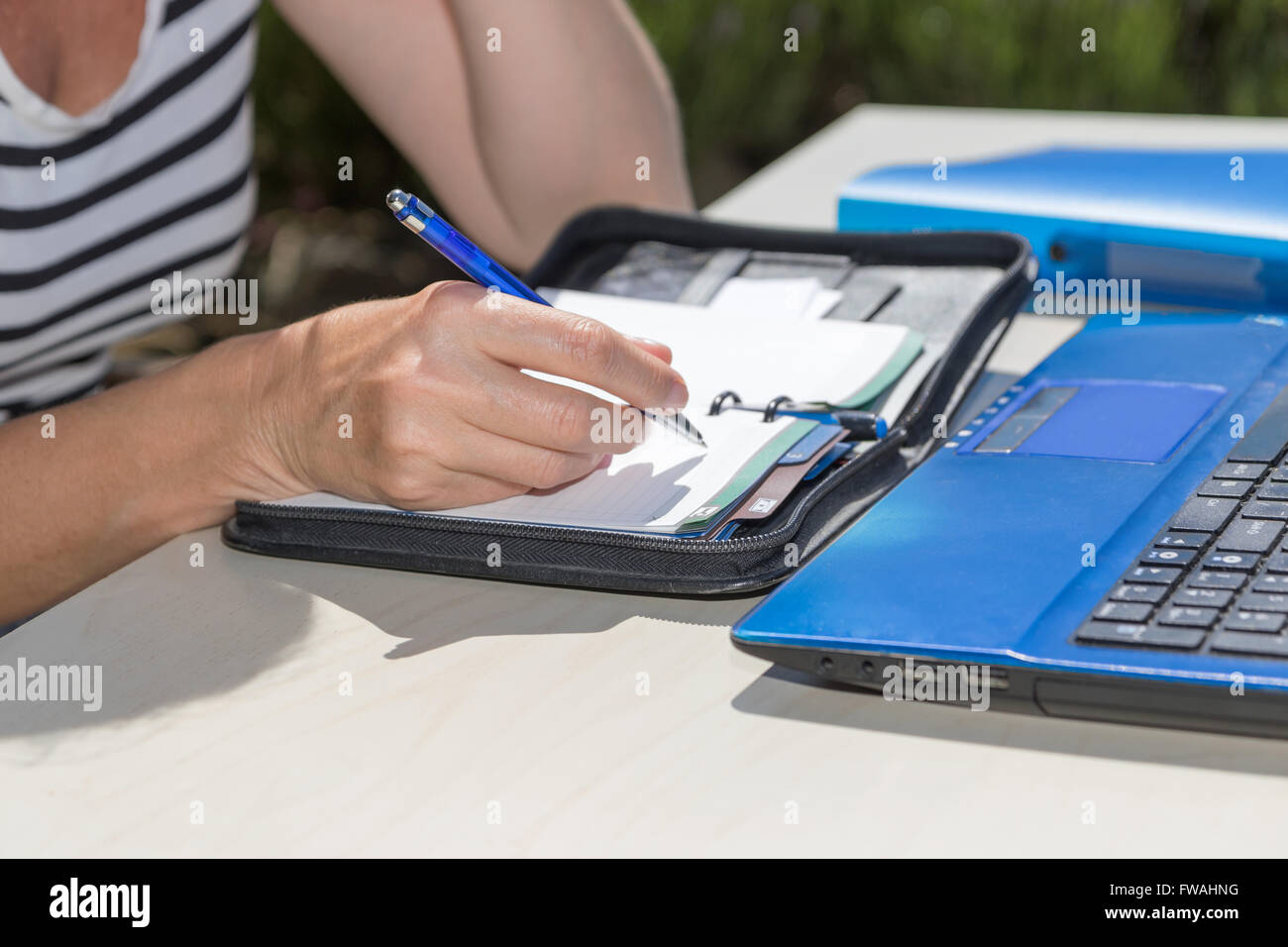 Primo piano di una donna e la scrittura a mano da penna blu per la carta diario. Aprire il notebook sul tavolo. Foto Stock