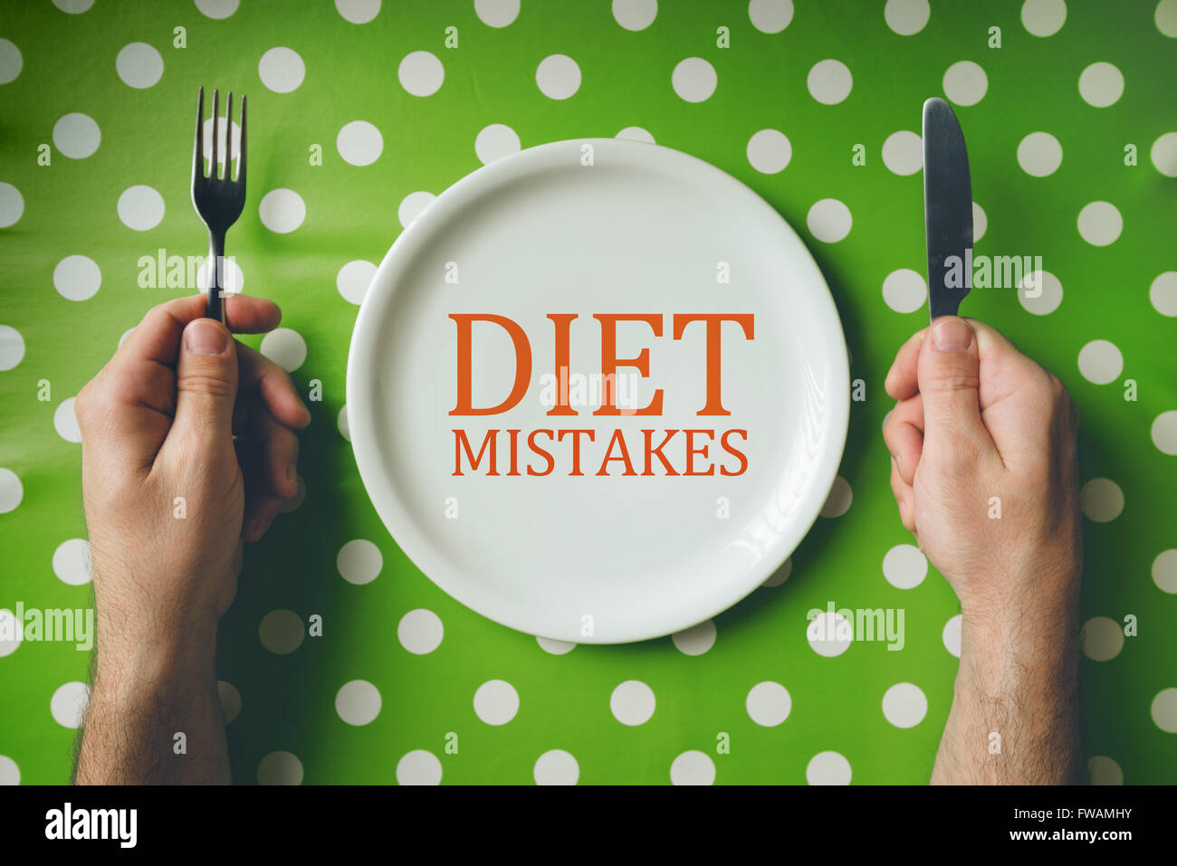 La dieta errori concetto, vista dall'alto del tavolo da pranzo con maschio mani forchetta e coltello su vuoto piastra piana. Foto Stock