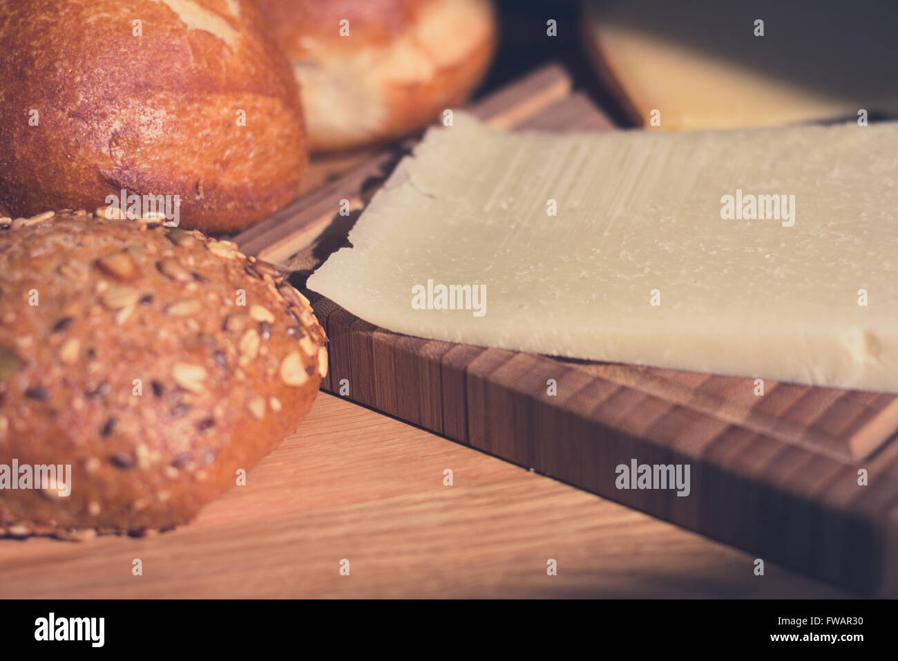 Pezzo di formaggio sulla tavola di legno e ciambelle di pane macro Foto Stock