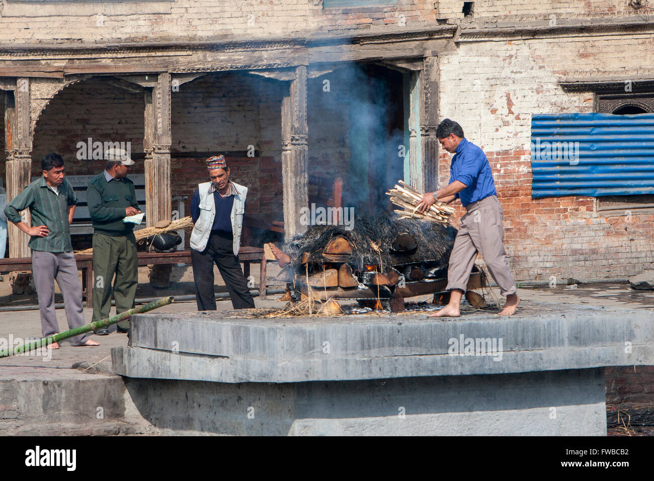 Il Nepal, Pashupatinath. Fasi di cremazione. L'aggiunta di pezzi di legno di un incendio già iniziato. Foto Stock
